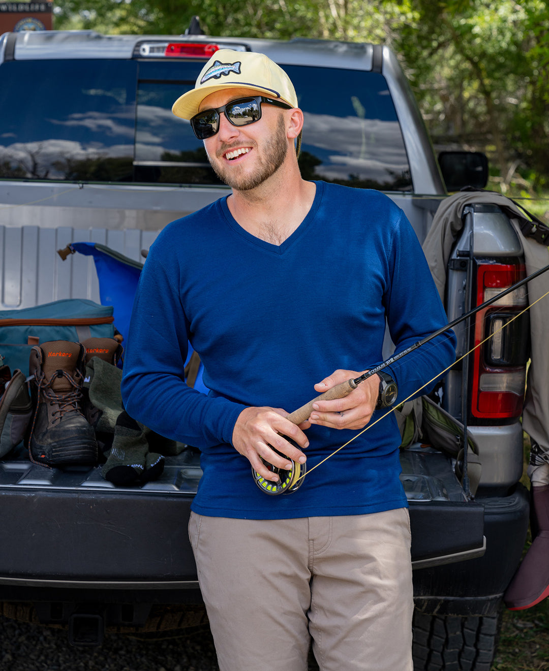 man wearing navy blue vneck leaning against a truck with a fishing pole