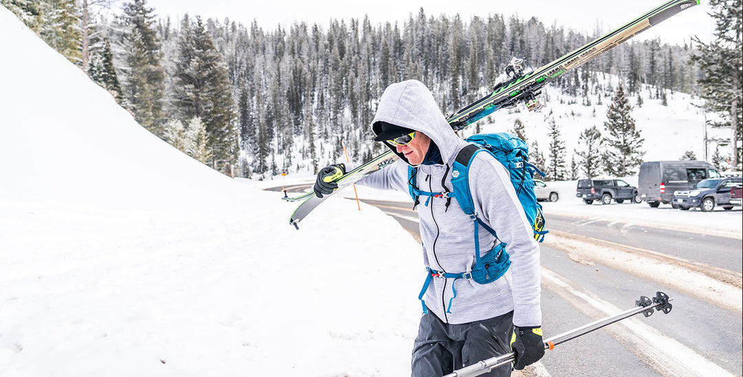 Man walking with his skis wearing an expedition weight hoodie