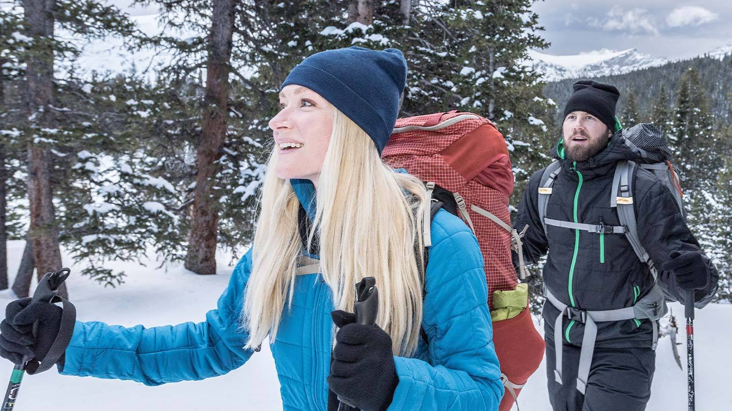 man and woman snowshoeing while wearing minus33 merino wool beanie, jacket, gloves and  base layers