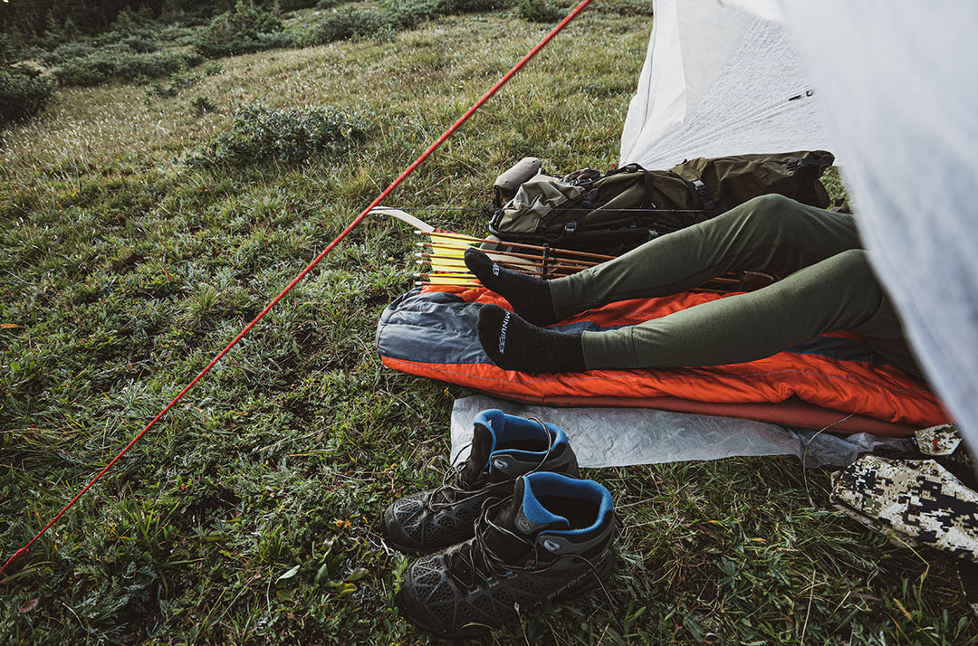 Man putting base layer wool bottoms on at camp site