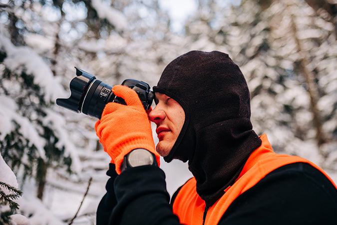 man taking photos of snowy trees wearing blaze orange glove liners