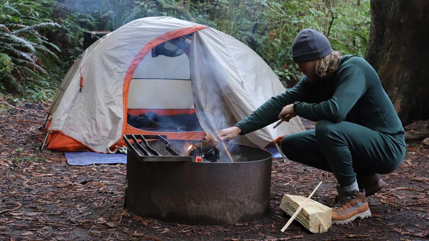 man stoking campfire wearing minus33 merino wool base layer outfit
