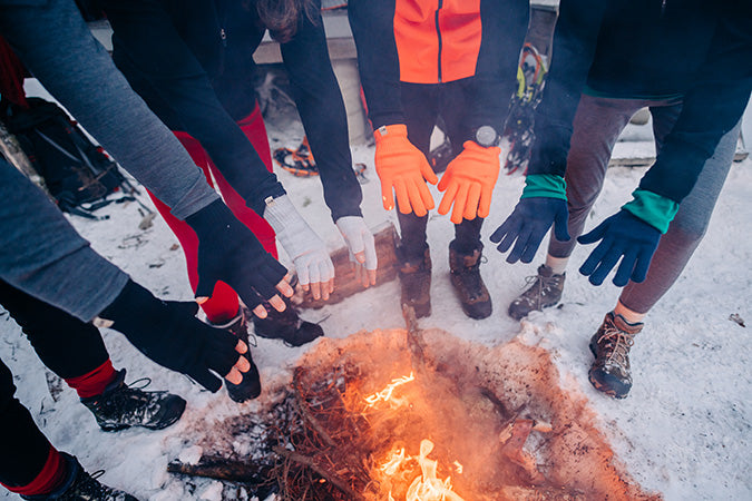 group of people with fingerless gloves and glove liners around a fire in the winter