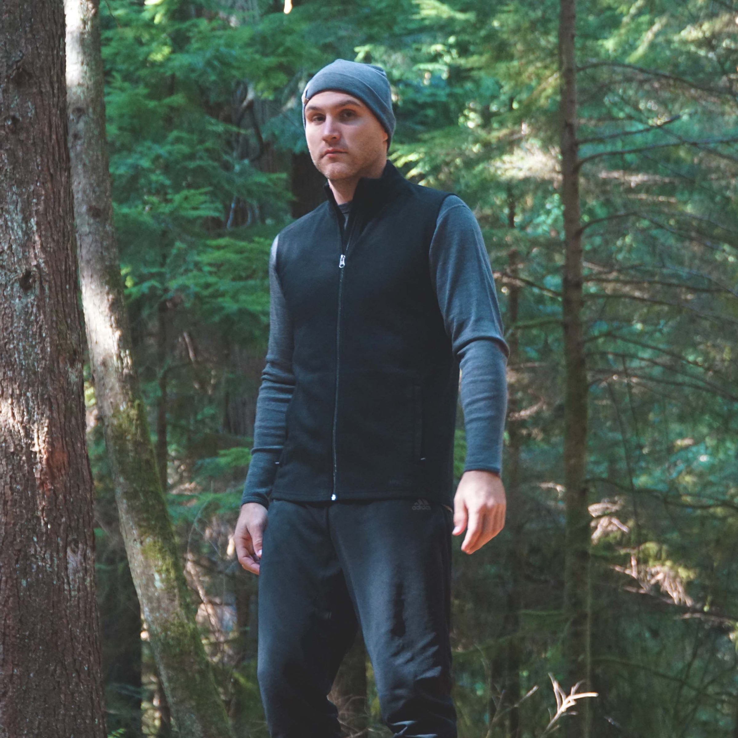 man in the woods wearing midweight long sleeve shirt with expedition weight vest and ridge cuff beanie