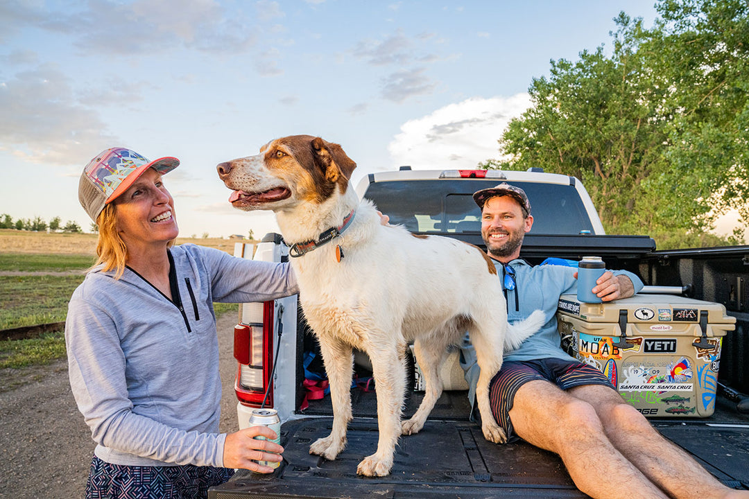 couple with dog on a tailgate wearing sun hoodies