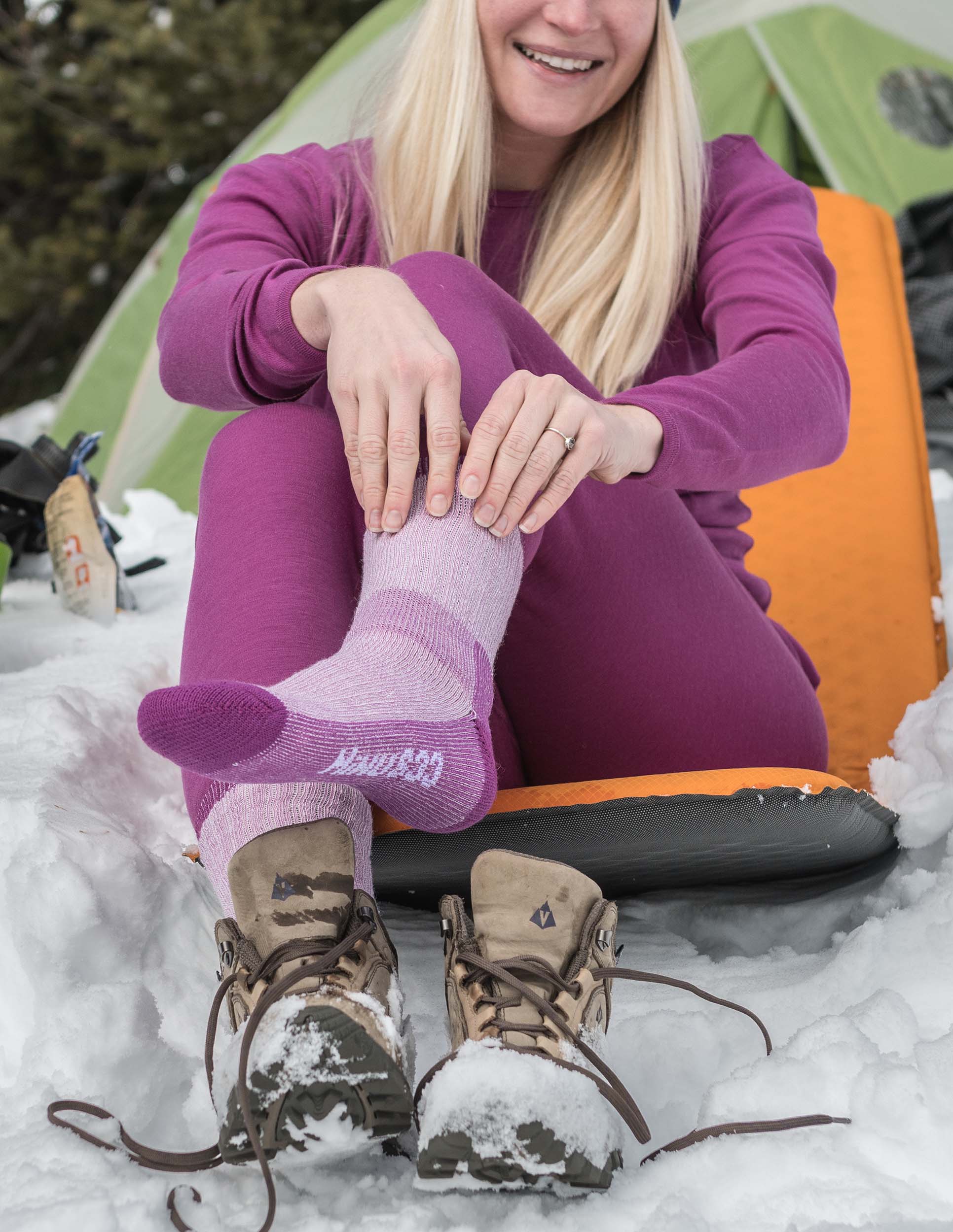woman hiking in the winter sitting on sleeping bad with radiant violet midweight base layers