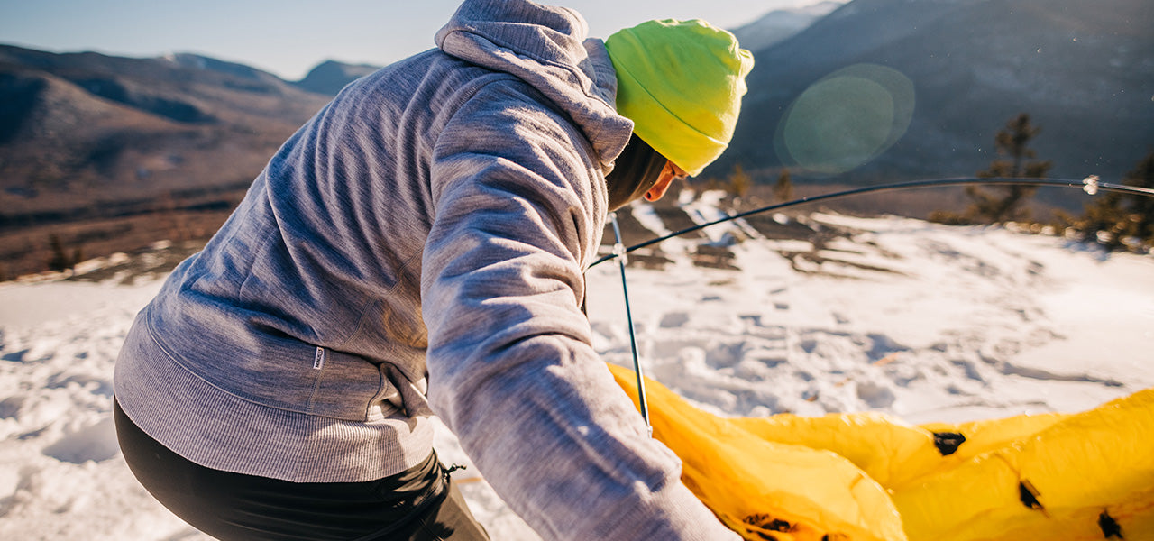 man setting up a tent on top of a mountain wearing expedition weight kodiak fleece hoodie