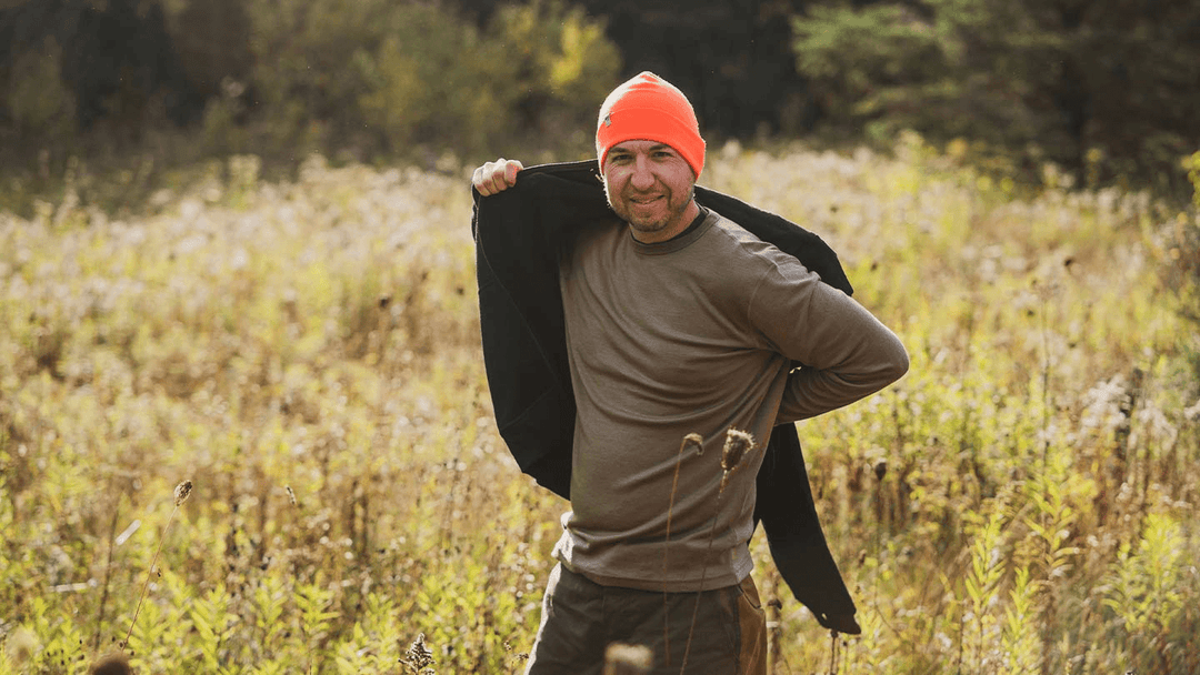 man in field putting on minus33 merino wool expedition sweatshirt over his lightweight crew base layer shirt