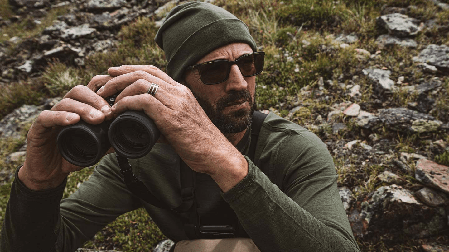 man with binoculars while wearing minus33 merino wool midweight long sleeve crew and beanies