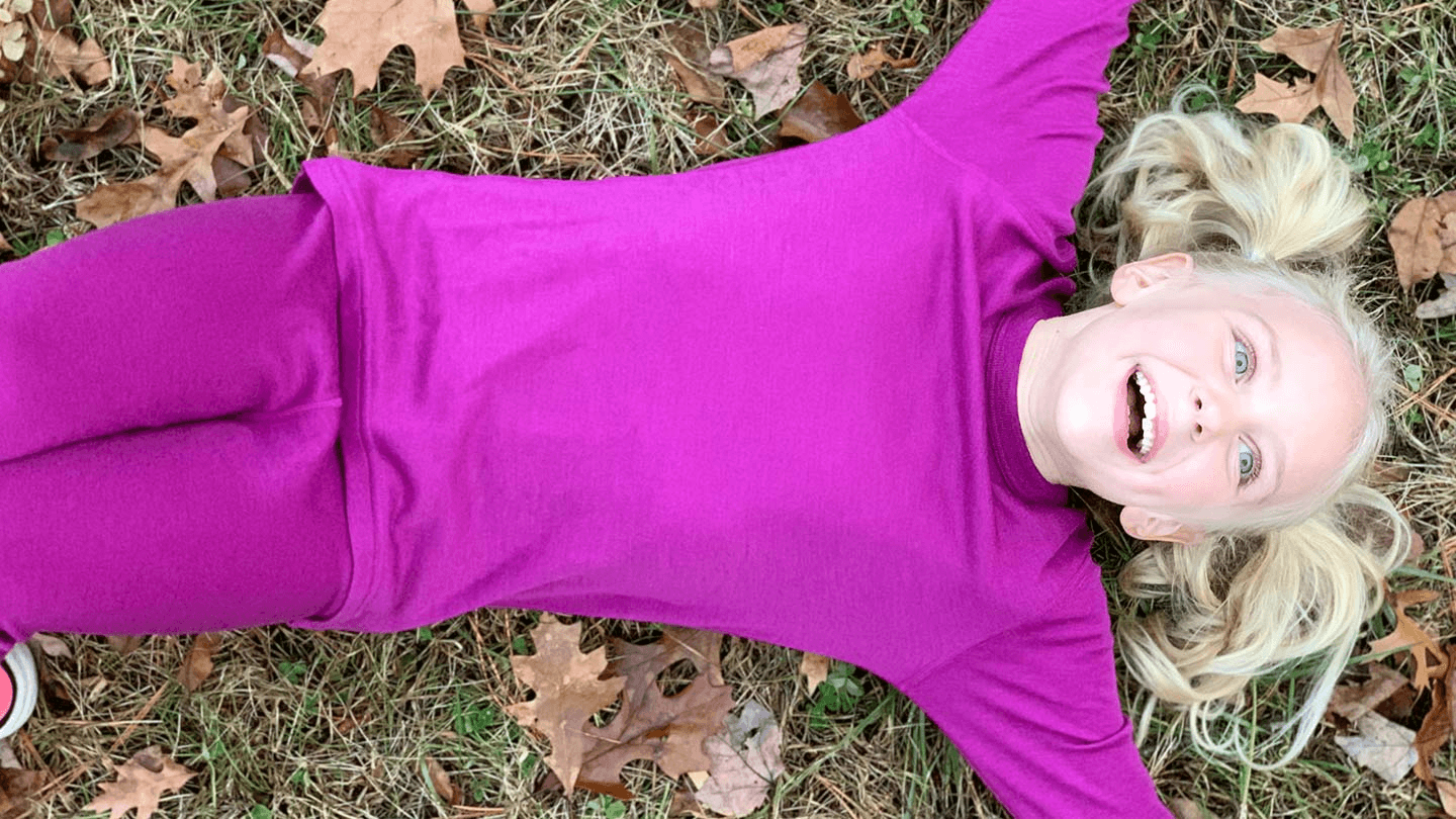 young girl laying in pile of leaves wearing minus33 merino wool base layer top and bottom set for kids