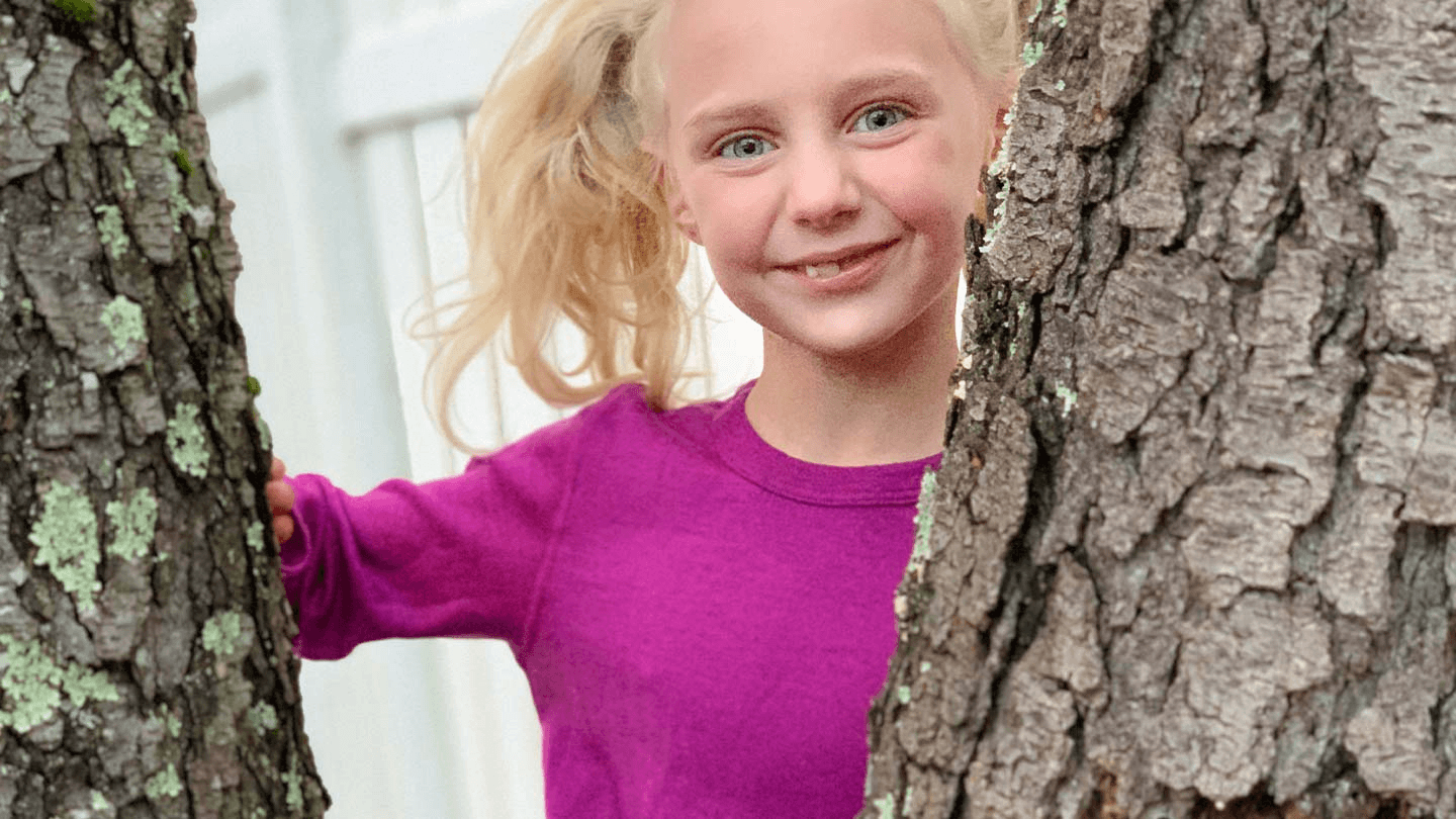 young girl climbing tree while wearing minus33 merino wool base layer set for kids