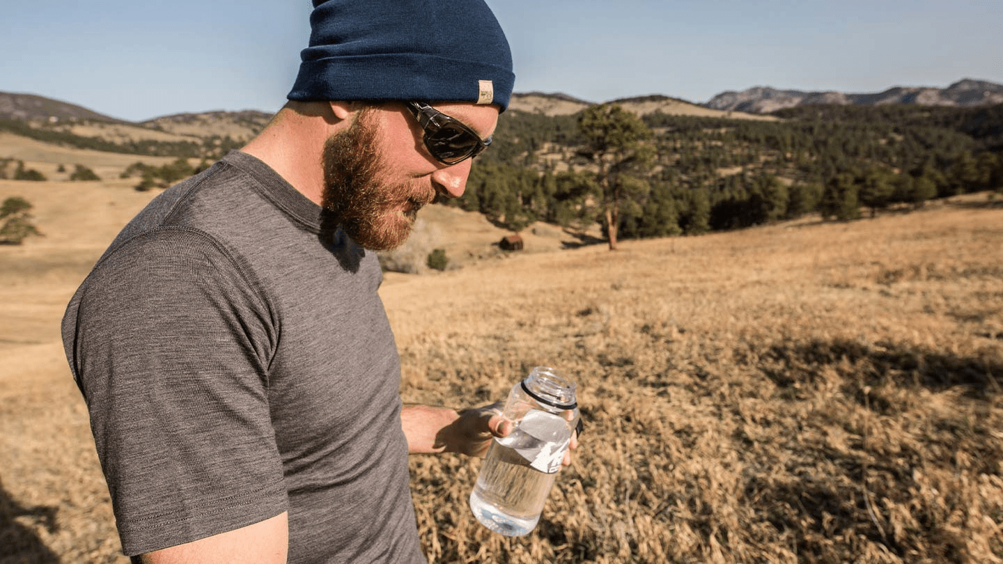 man hiking and drinking water while wearing minus33 merino wool lightweight t-shirt and beanie