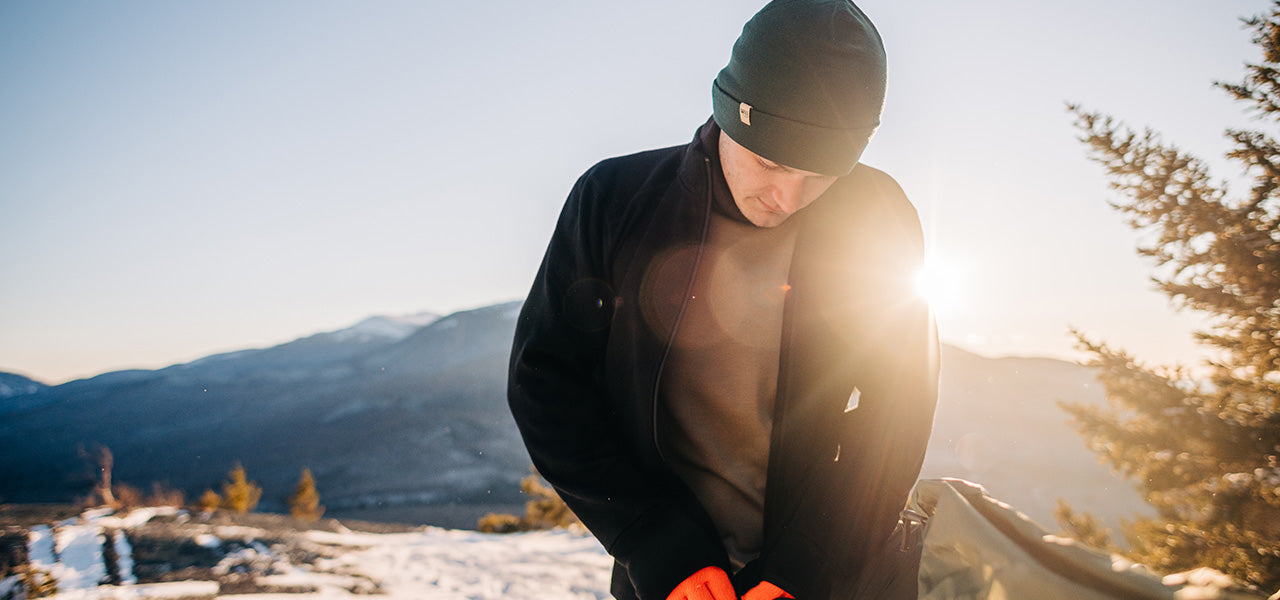 man zipping up outer layer while  wearing a midweight base layer shirt on top of a mountain in the winter