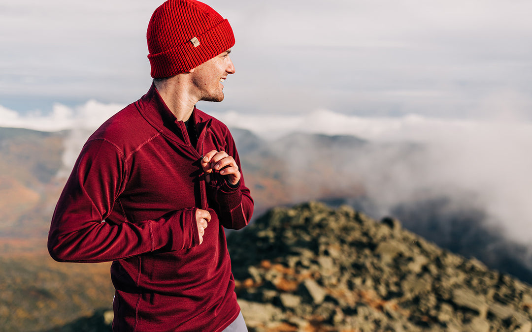man hiking in the fall wearing midweight merino wool maroon quarter zip with red beanie