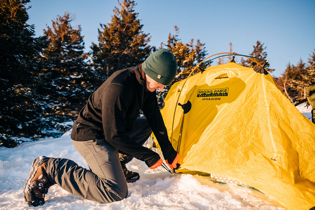 expedition weight merino wool man setting up a tent on top of the mountain wearing a heavyweight zip up