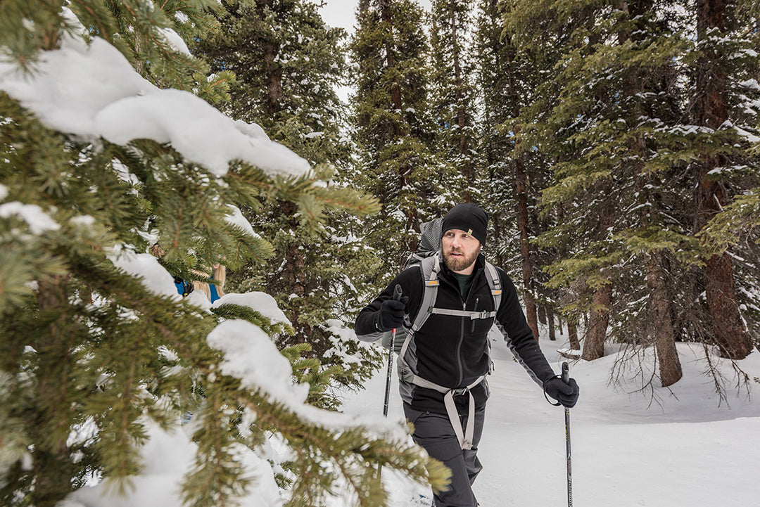 man snowshoeing in the woods wearing merino wool full zip midweight hoodie