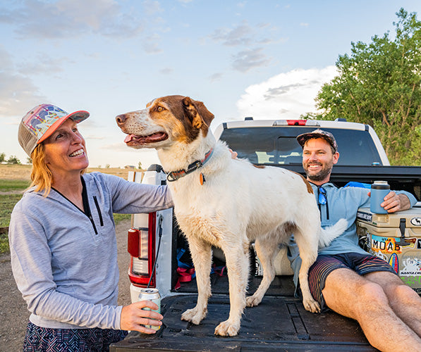 couple sitting on the bed of the truck with their dog wearing a merino wool micro weight sun hoodie to stay cool from the heat