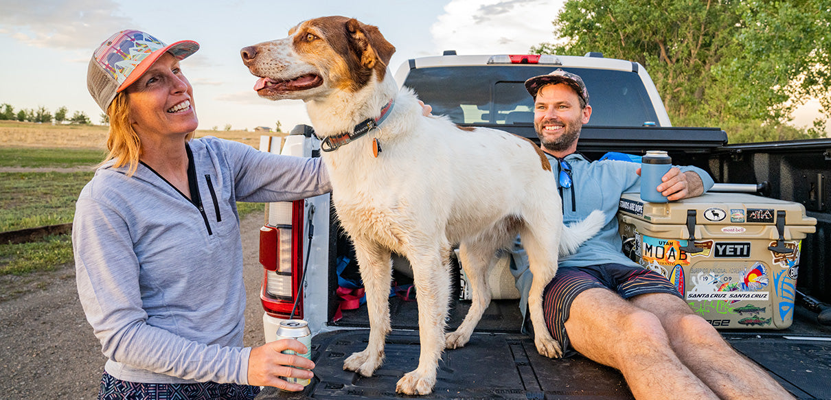couple sitting on the bed of the truck with their dog wearing a merino wool micro weight sun hoodie to stay cool from the heat